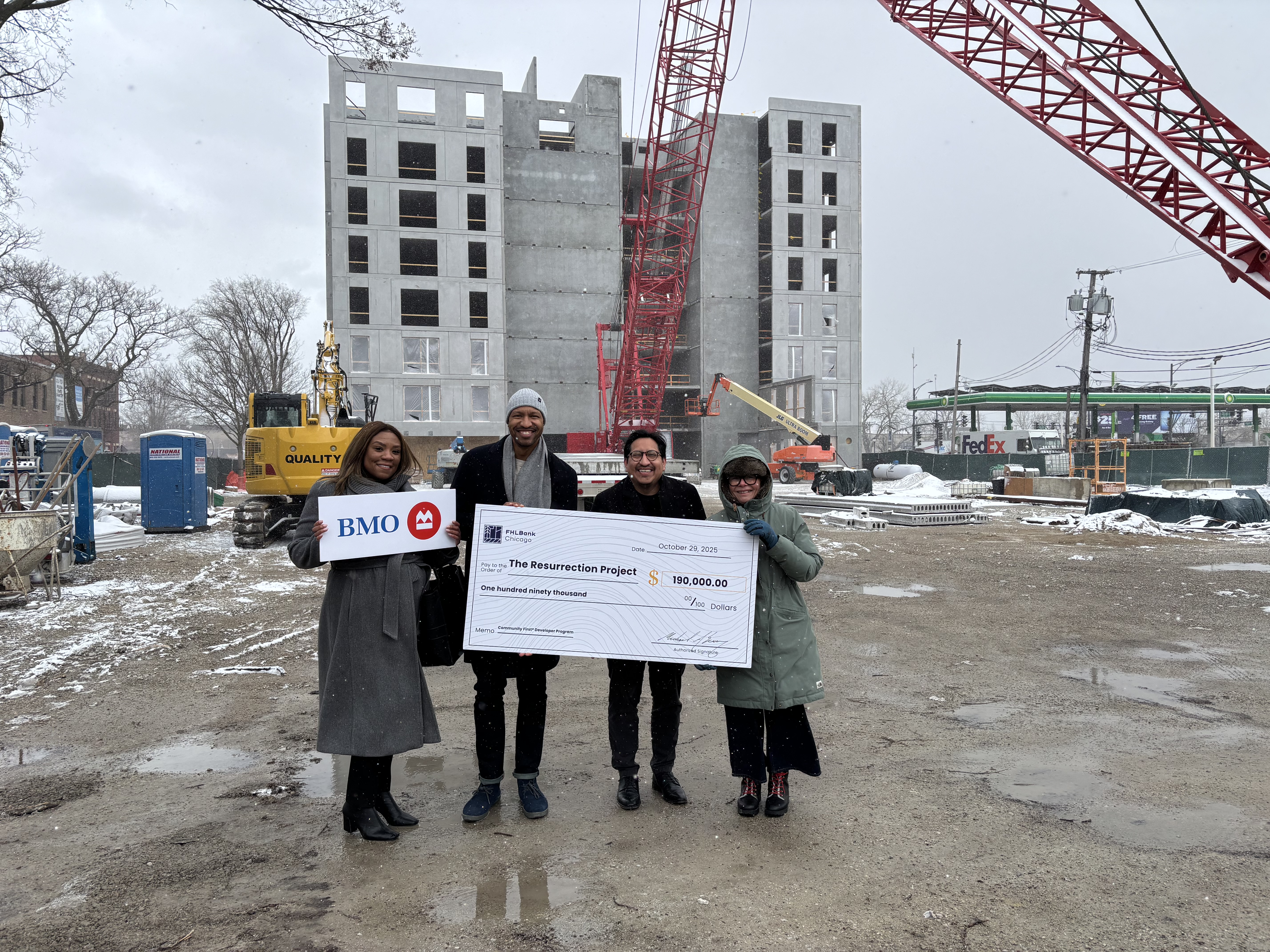 BMO + Resurrection Project Developer Check Presentation Four people stand at a construction site in the snow with a large check.