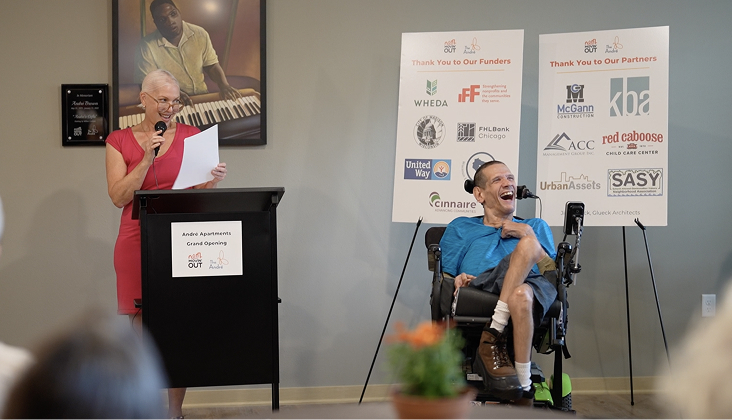 grants-funding Woman reading from a podium with man in a wheelchair next to her